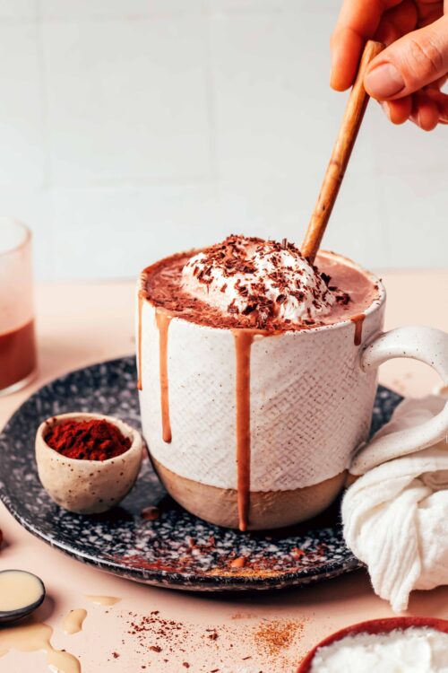 Using a small wooden spoon to stir a mug of tahini hot chocolate